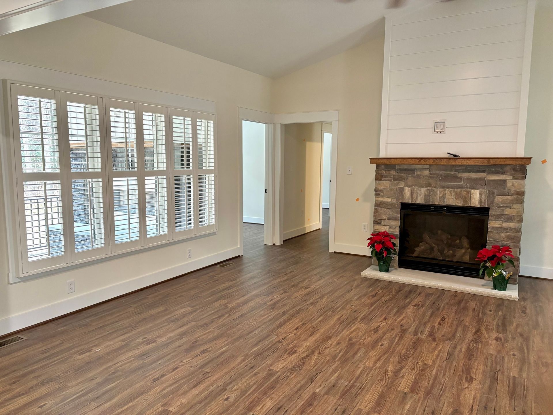 Empty living room with hardwood floors, bay windows, and a stone fireplace decorated with red flowers