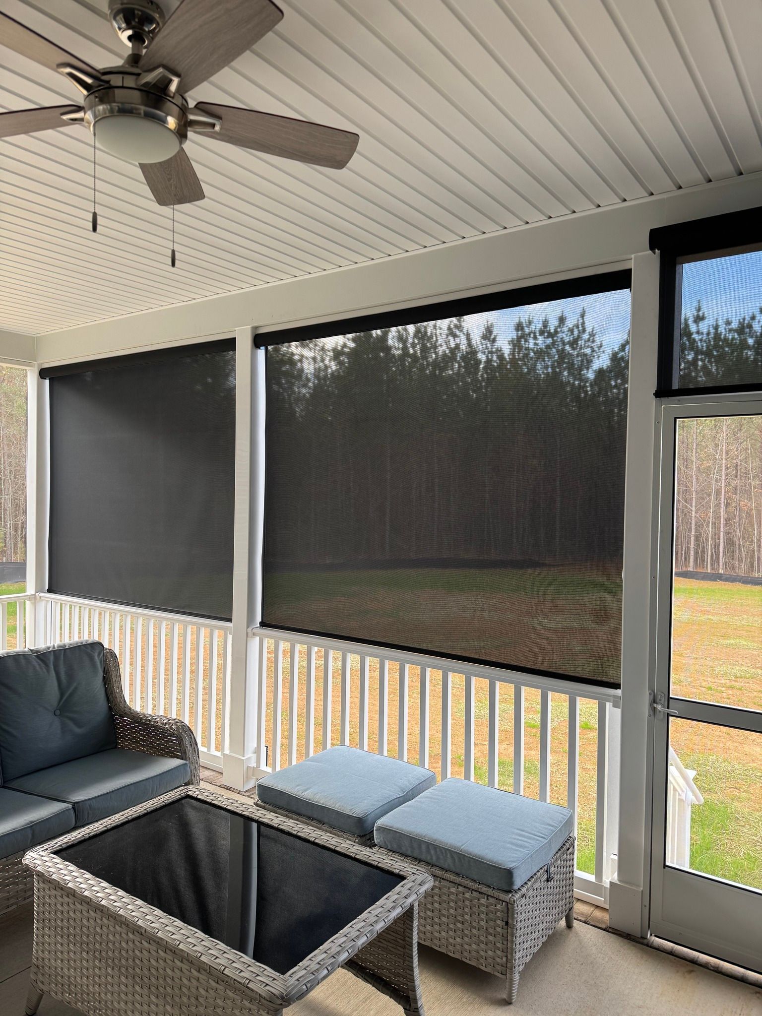Covered porch with wicker sofa and ottoman, ceiling fan, and screened view of trees and yard