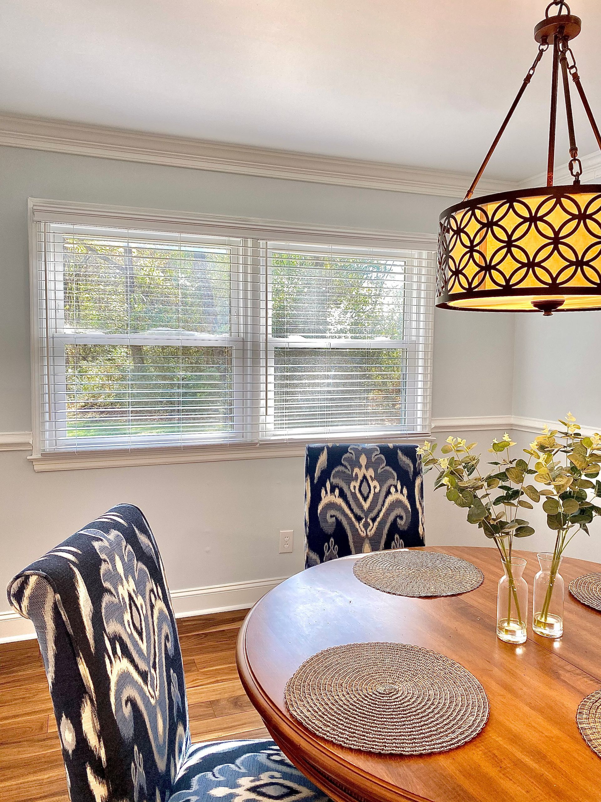 Bright dining nook with wooden table, patterned chairs, bay windows, and a hanging pendant light.