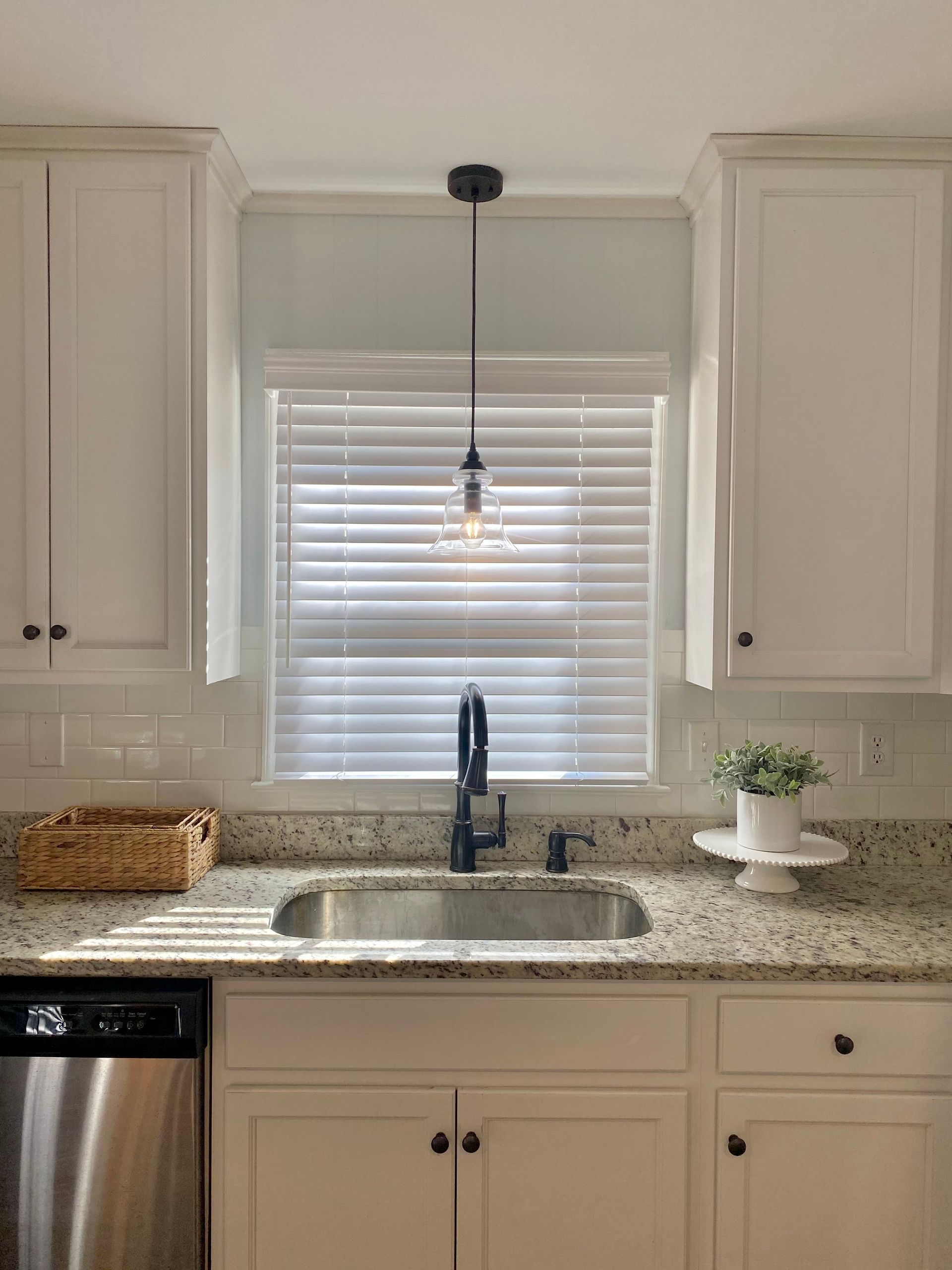 Bright white kitchen with window over sink, granite countertop, cabinets, and small plant.
