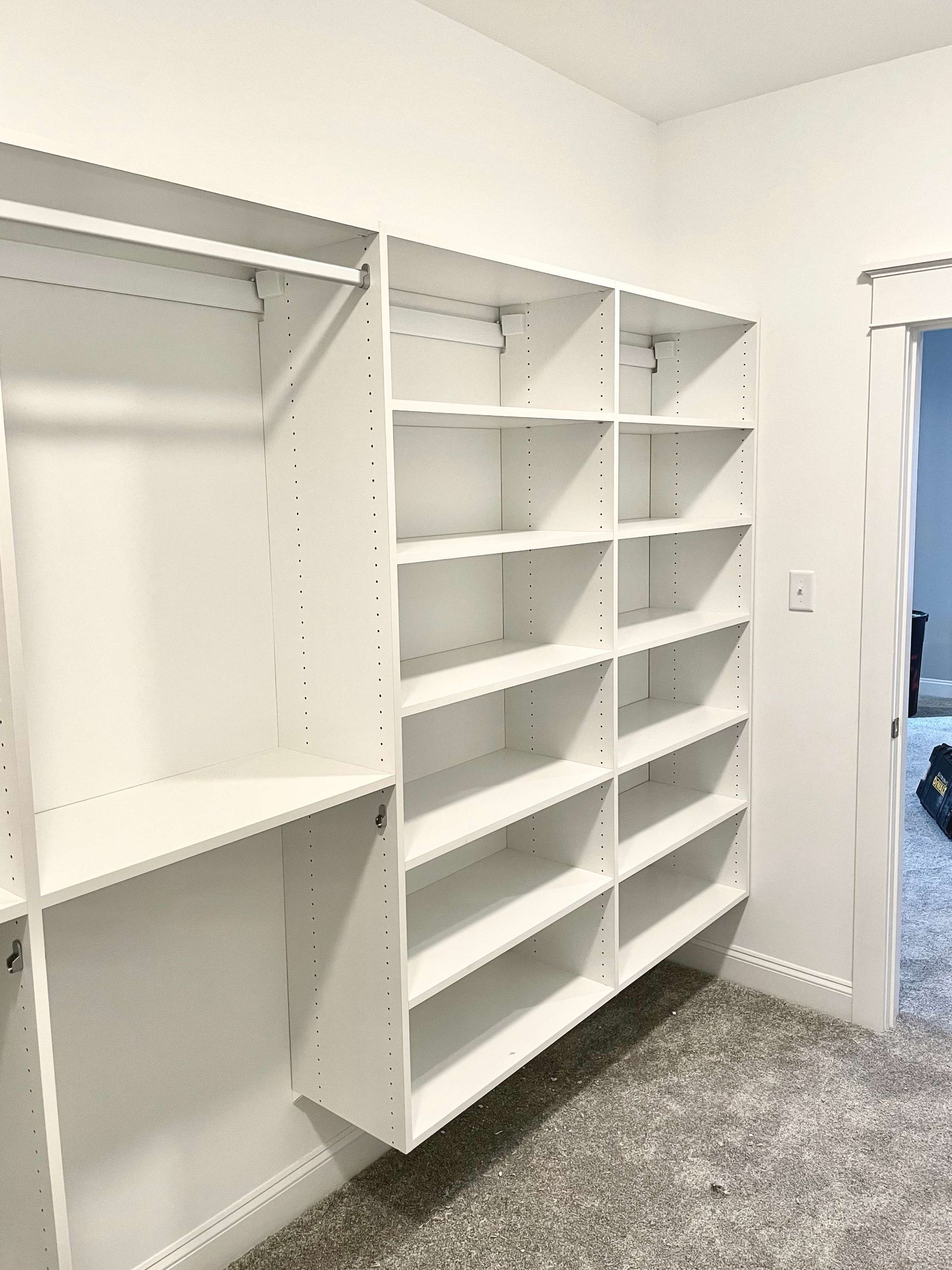 White walk-in closet with built-in shelves and hanging rods, empty except for a gray carpeted floor.