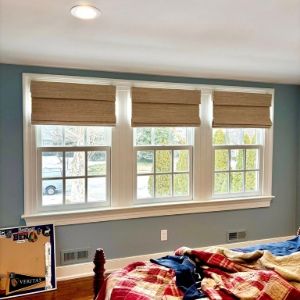 Bedroom with three windows and woven shades above a red plaid bedspread