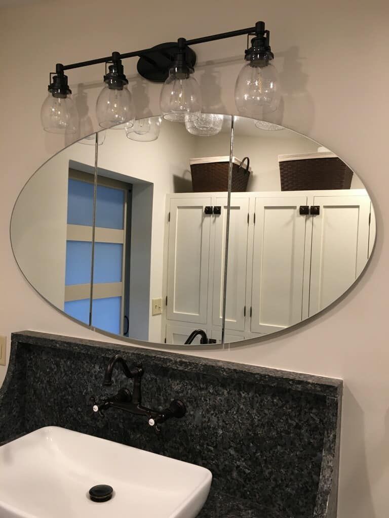 Bathroom vanity with oval mirror, black granite countertop, white sink, and three globe light fixtures above.