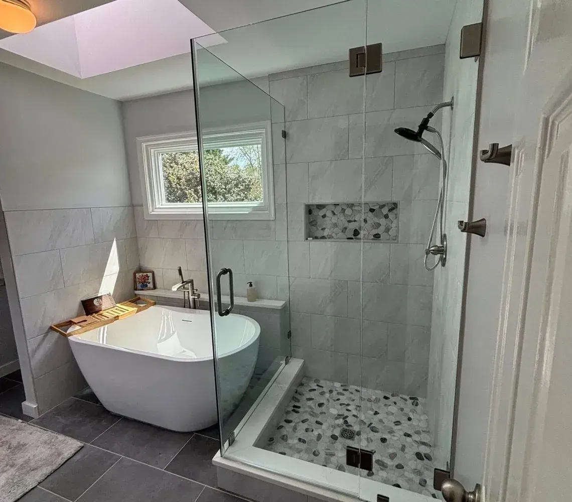 Modern bathroom with a freestanding tub, glass shower, gray tile floor, and skylight.