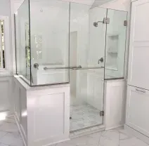Corner glass shower with black frame in a beige bathroom, beside a white sink and patterned rug