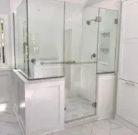 Corner glass shower with black frame in a beige bathroom, beside a white sink and patterned rug