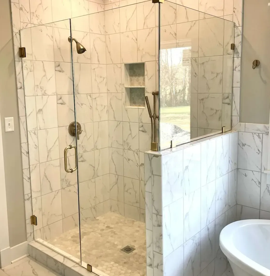 Glass-enclosed walk-in shower with marble tile, bench, and rainfall showerhead in a bright bathroom