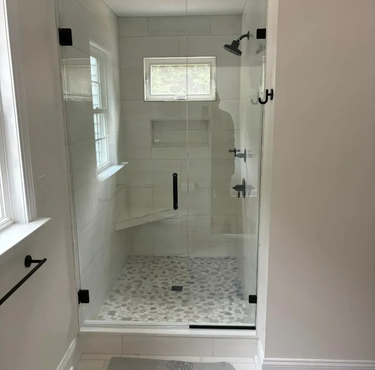 Modern bathroom shower with glass enclosure, white tile walls, and pebble-pattern floor.