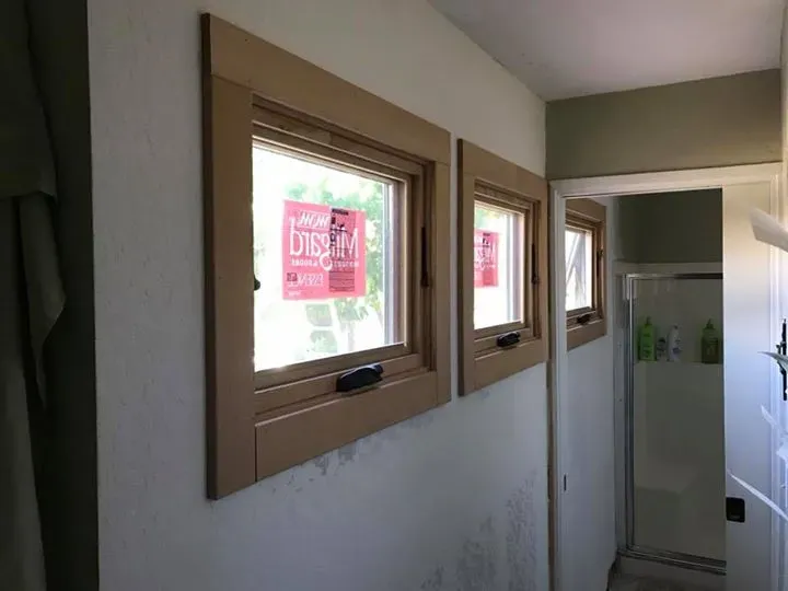 Two tan-framed windows on a light wall, next to a doorway. Bathroom partially visible through the doorway.
