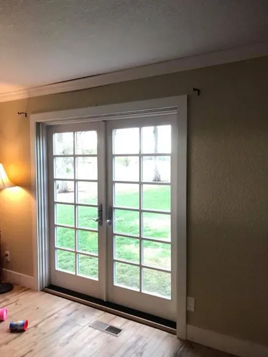 White-framed French doors, with multiple panes, open onto a grassy yard. Cream walls, wood floor.