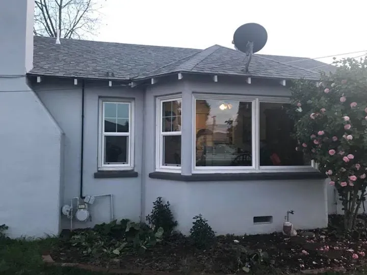 Gray house exterior with bay window and satellite dish. Landscaping and a chimney are also visible.