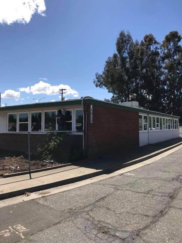 School building with brown and white exterior, chain link fence, and tall trees.