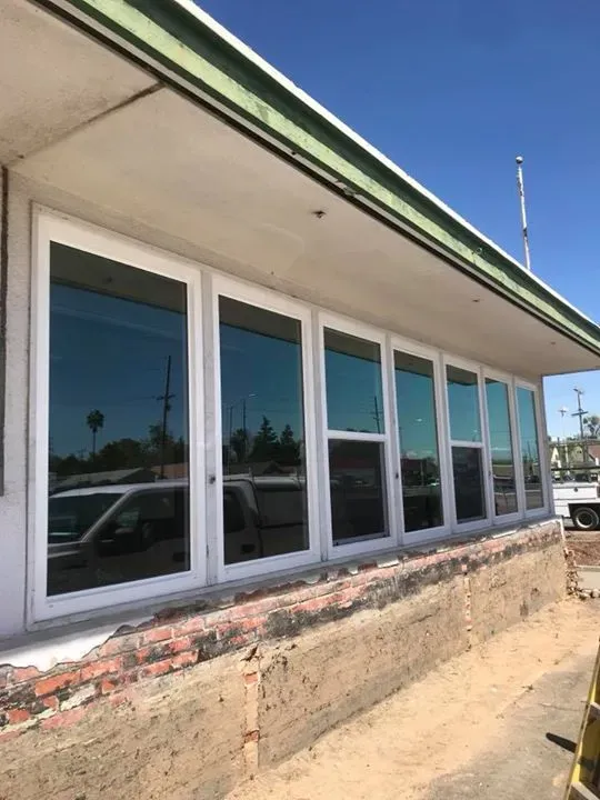 Row of tall, white-framed windows on a building with a brick foundation and green trim against a clear, blue sky.