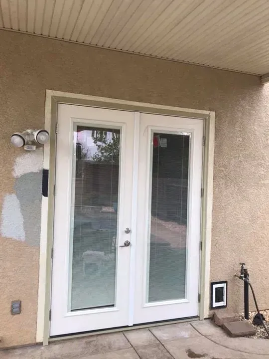 White French doors with glass panes, beige stucco wall, and outdoor setting.