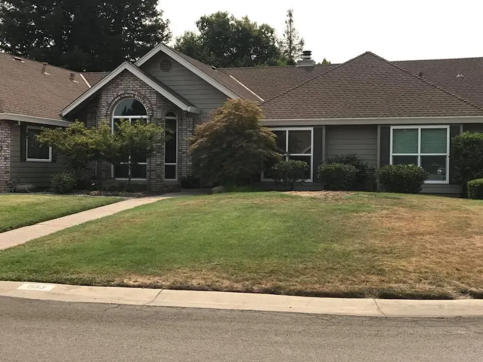 Suburban house with gray siding, arched window, and brown roof, set on a green lawn.