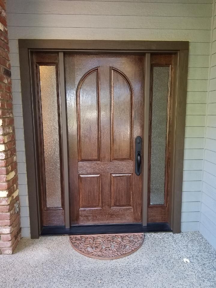 Wooden front door with arched top and side panels of textured glass; brown frame and doormat.