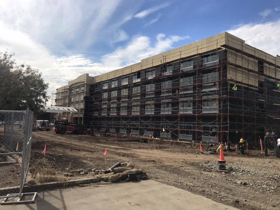 Building under construction, scaffolding covers exterior, dirt and construction equipment in front.