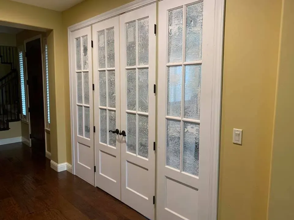 Four white paneled doors with textured glass, black hardware, against yellow walls and dark wood floor.