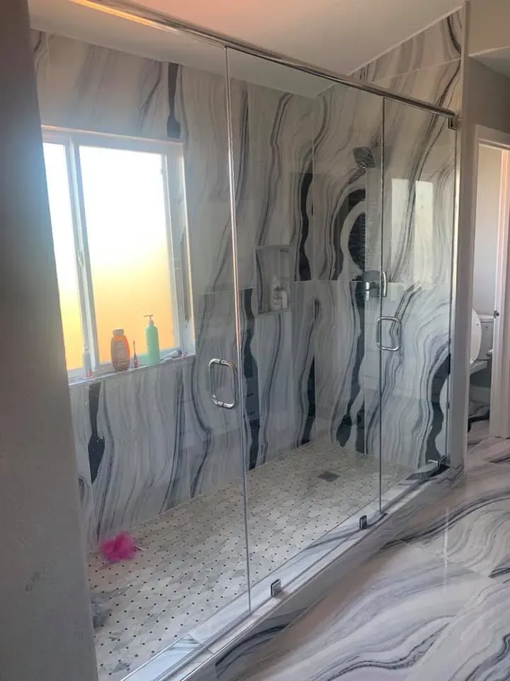 Modern bathroom with marble-patterned walls and a glass-enclosed shower next to a window.