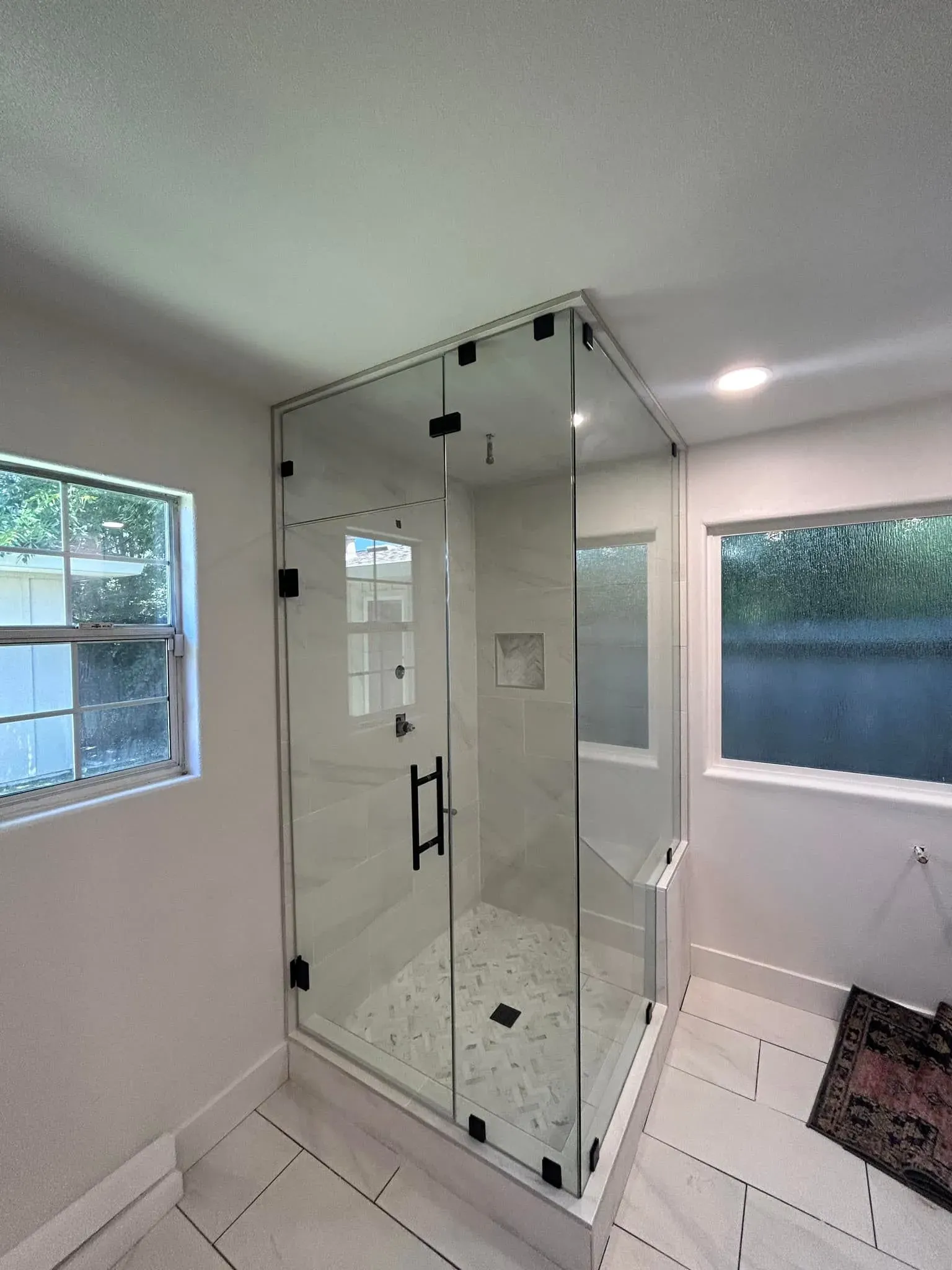 A corner glass shower with white tile interior, black hardware, and two windows.