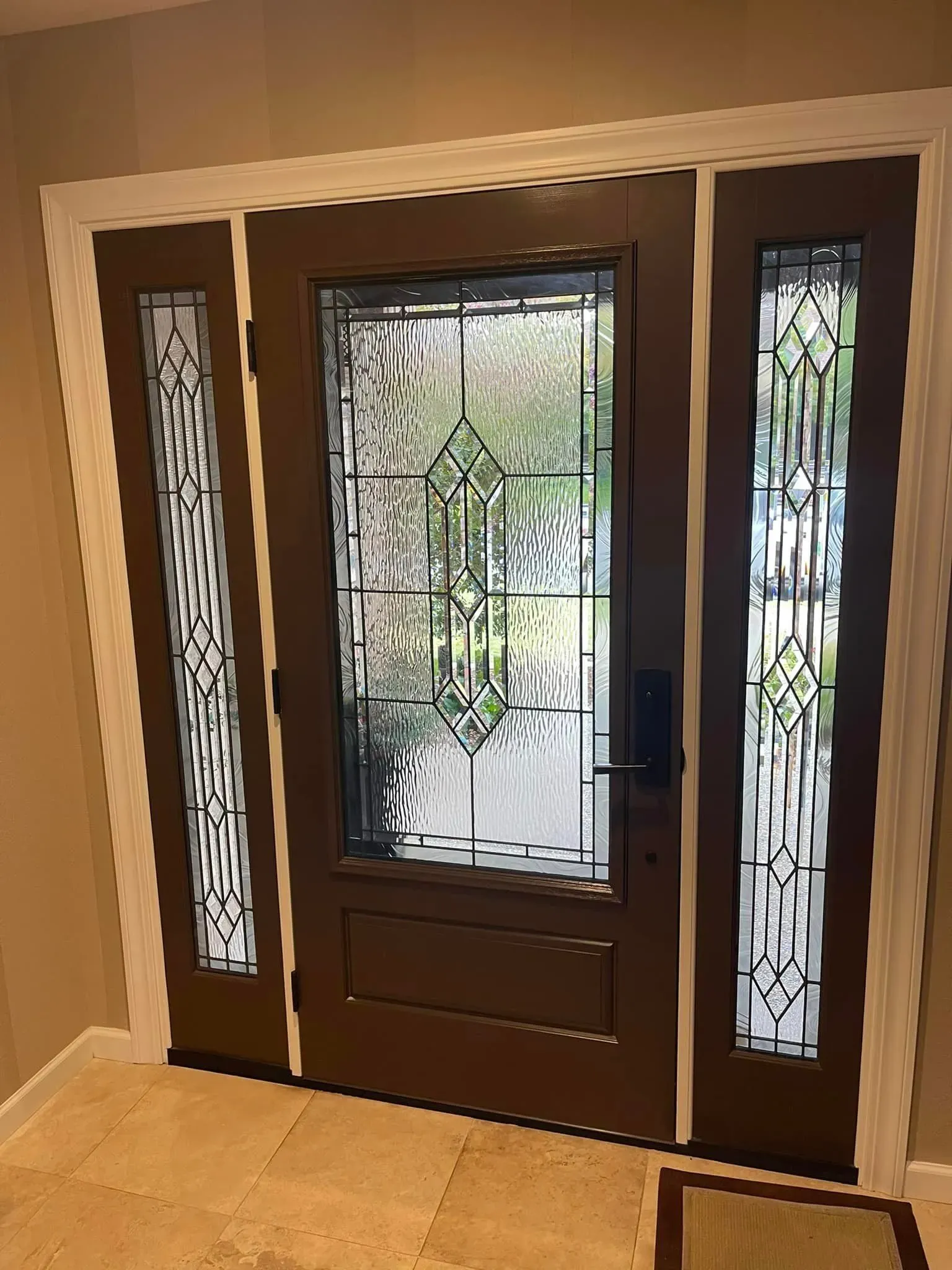 Brown front door with decorative stained glass panels, white trim, and a neutral tile floor.