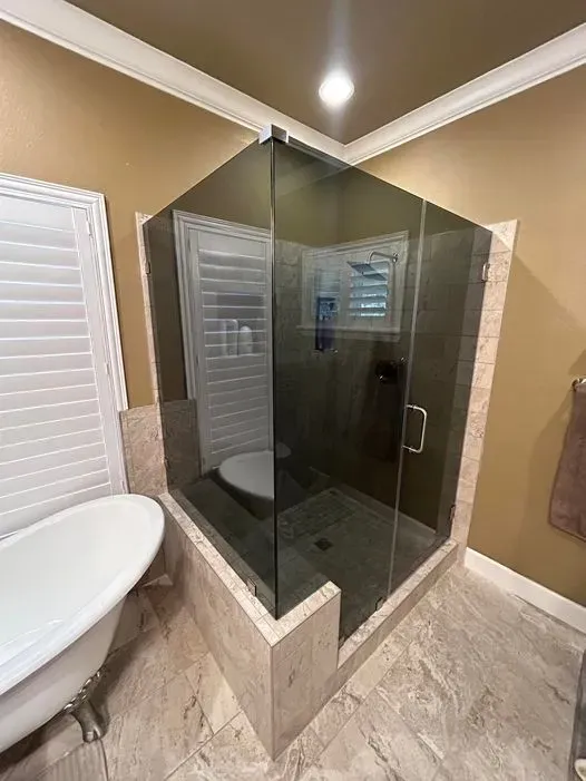 Corner shower with dark tinted glass, tan tile, and a white bathtub.