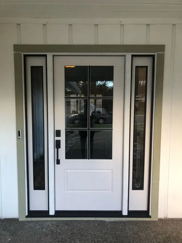 White front door with sidelights, black hardware, surrounded by light green trim, gray concrete.