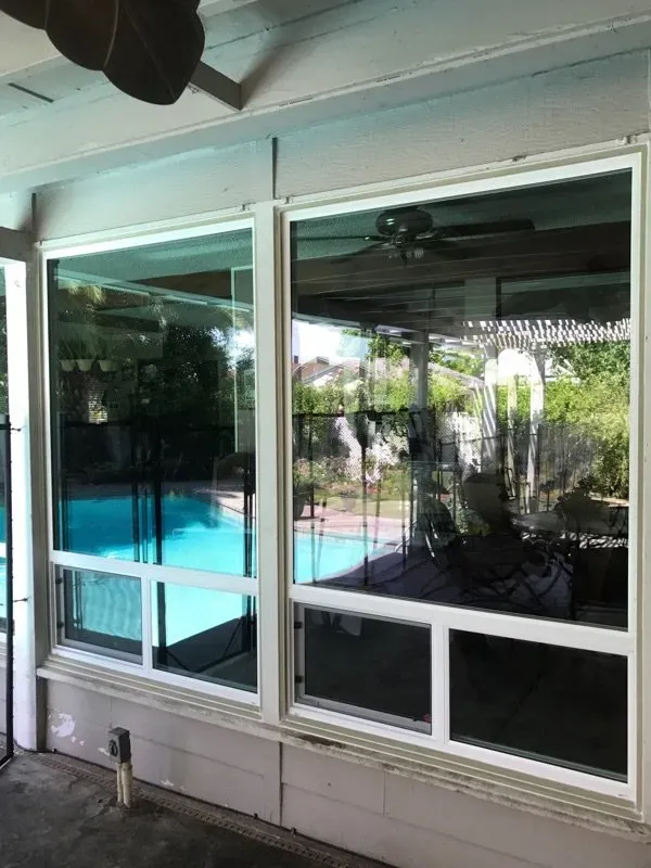 Two white-framed windows reflecting a pool and outdoor area.