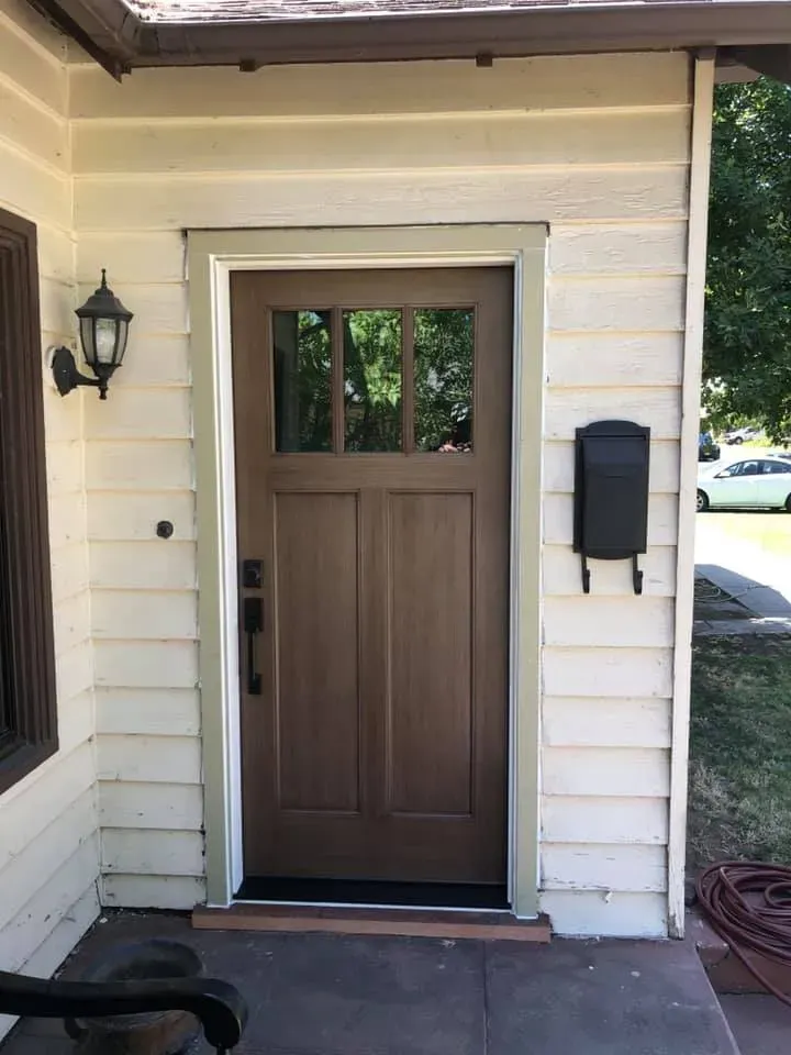 Brown front door with glass panels and sidelight, with black mailbox on cream-colored siding.