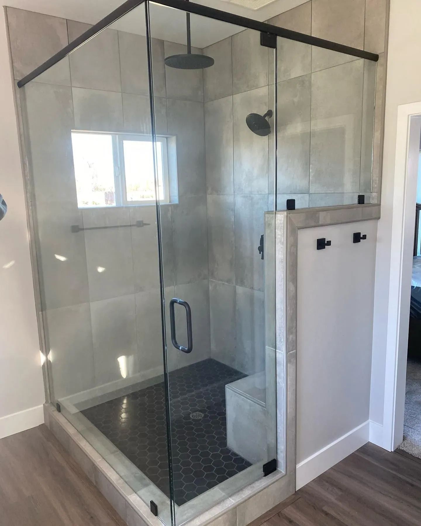 Modern shower enclosure with glass doors, black hardware, and gray tiled walls and floor.