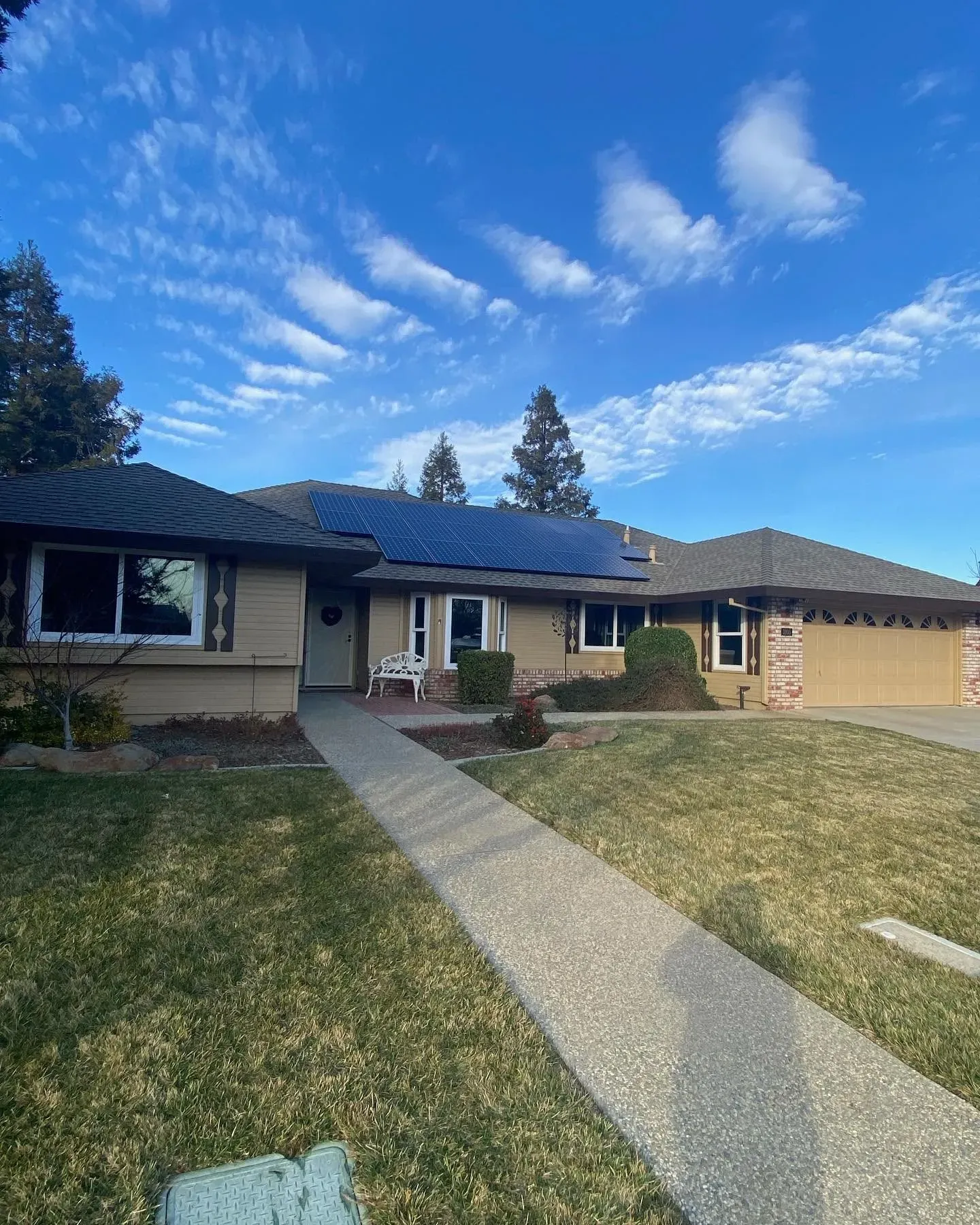 House with solar panels on roof, pathway leading to the front door, blue sky with clouds.