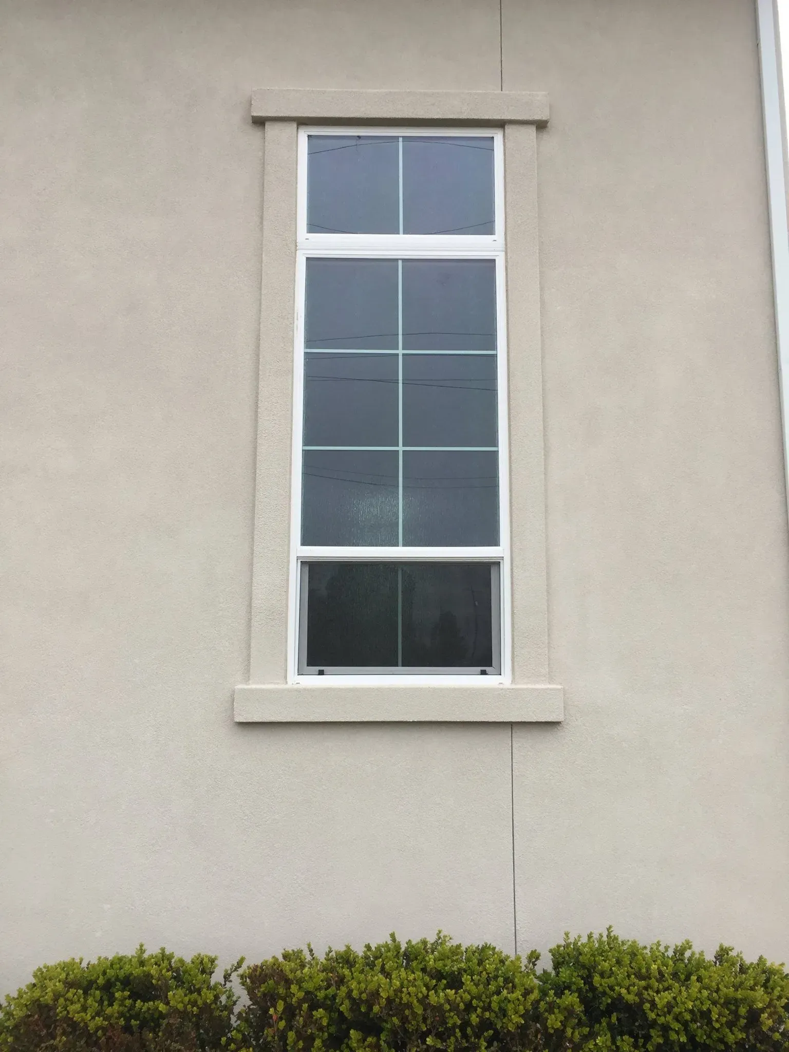 Tall, white-framed window with grid, set in light beige stucco wall with a decorative frame.