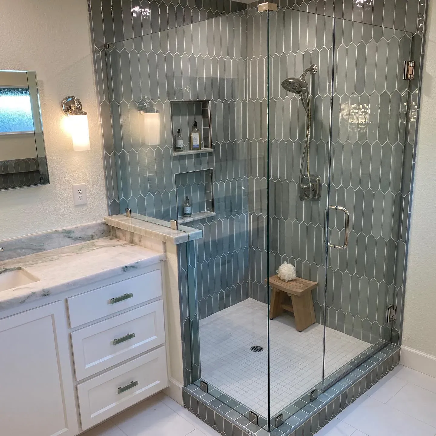 Modern bathroom with a glass-enclosed shower, featuring blue tile and a built-in shelf.