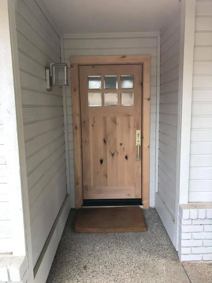 Wooden front door with glass panels, tan doormat, white siding and trim.