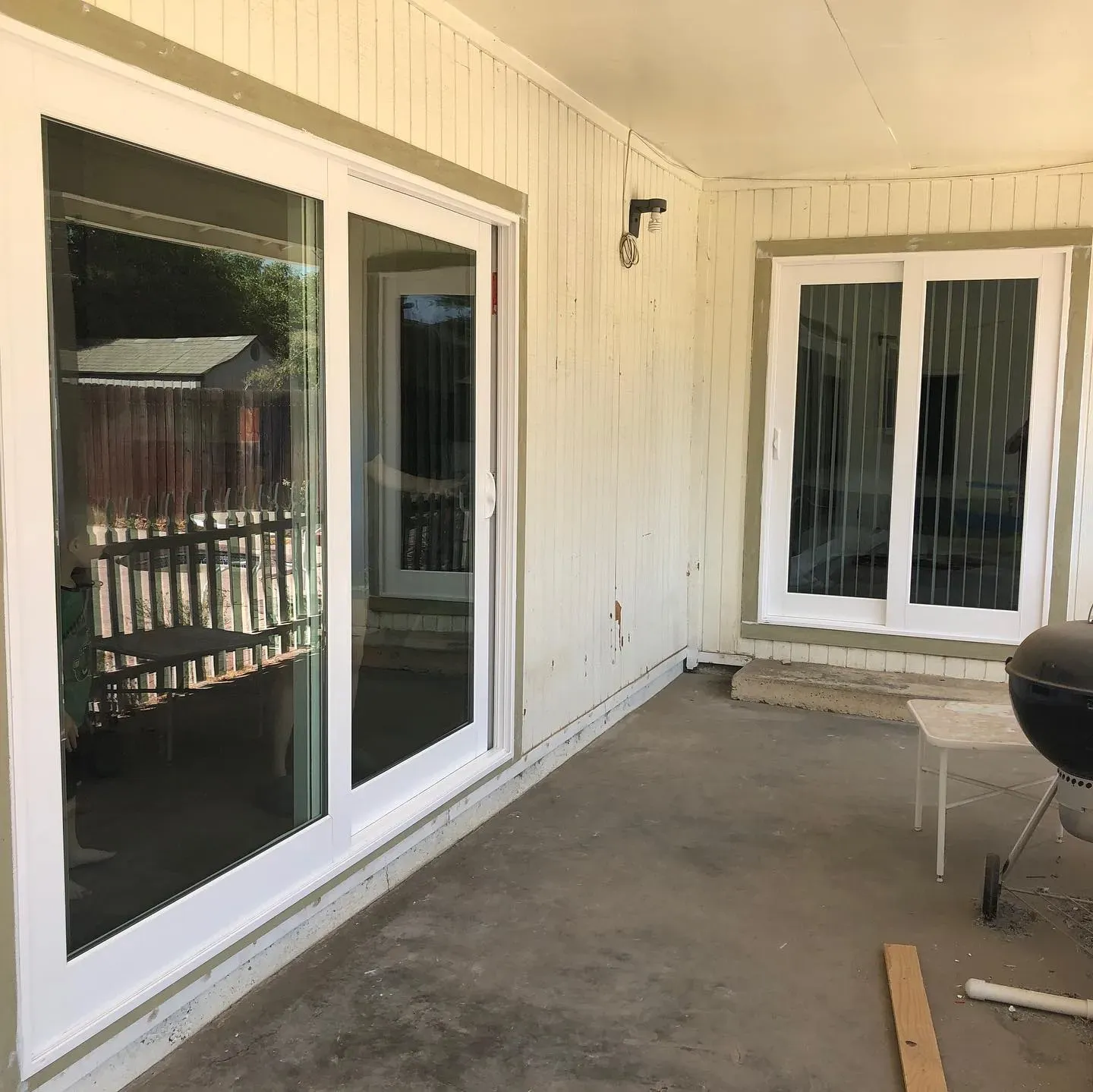 White-framed sliding glass doors on a covered porch with concrete flooring and a small grill.