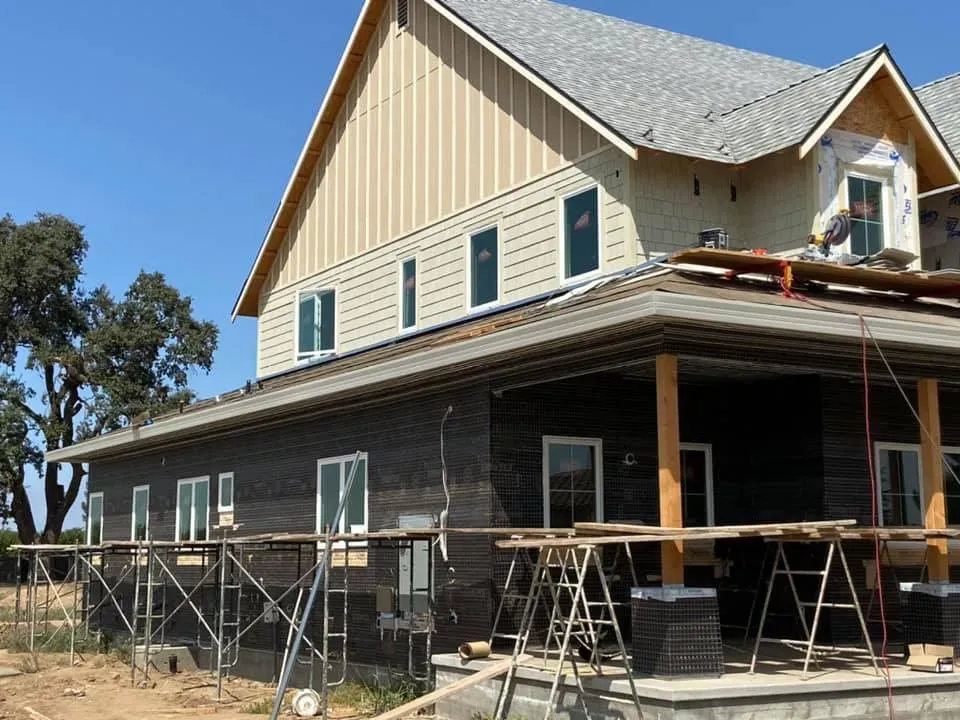 House under construction with siding and windows, scaffolding, and porch.