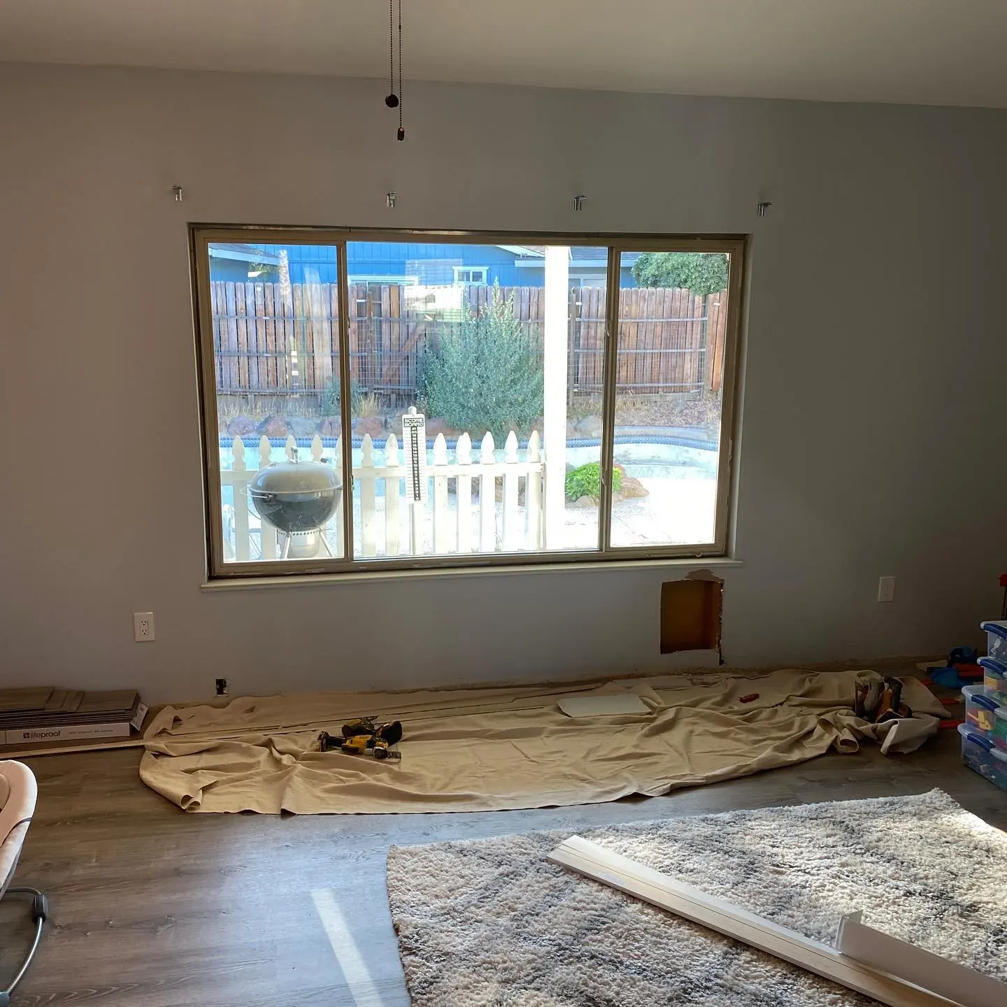 Interior room with a large window, covered floor, and exposed wall damage.