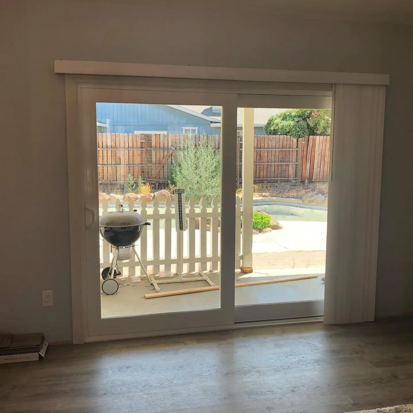 Sliding glass door leading to a backyard with a grill, fence, and trees.