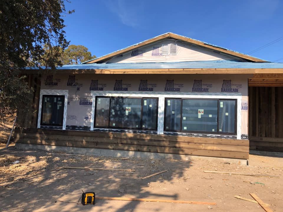 Exterior of a house under construction; windows and wooden siding installed, blue tarp on roof.