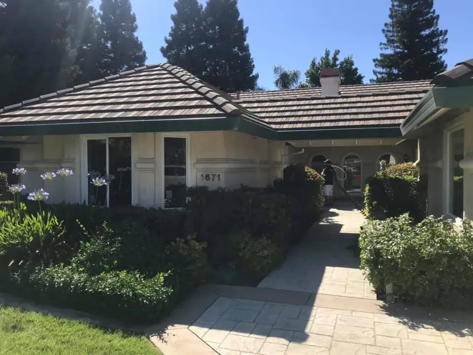 Beige house with a tiled roof, green trim, and landscaping. A walkway leads to the entrance.