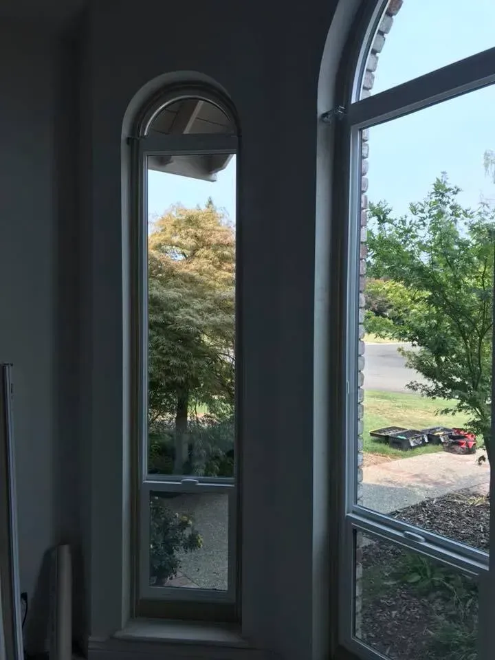 Interior view: Tall, arched window reveals trees and blue sky. Adjacent white-framed window.