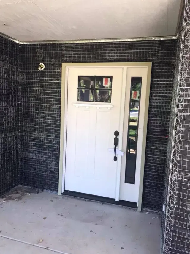 White front door with sidelight and black mesh siding. Gray porch.