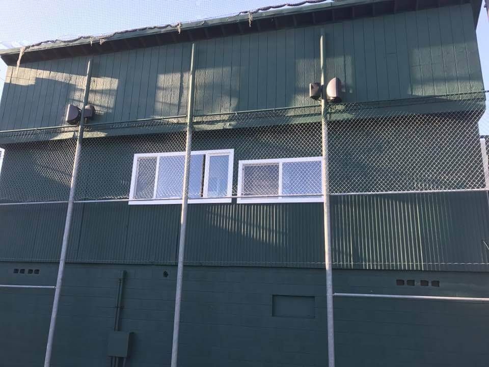 Green baseball dugout with windows, lights, and a protective fence.