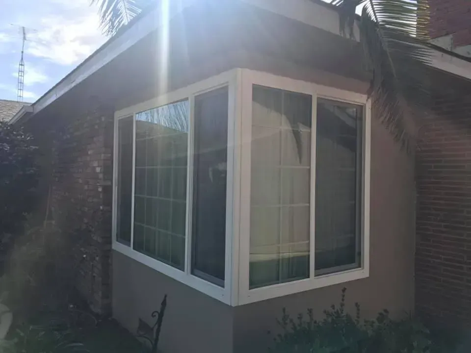 Corner of a house with white-framed windows. Sunlight shines brightly. Brick and stucco exterior.