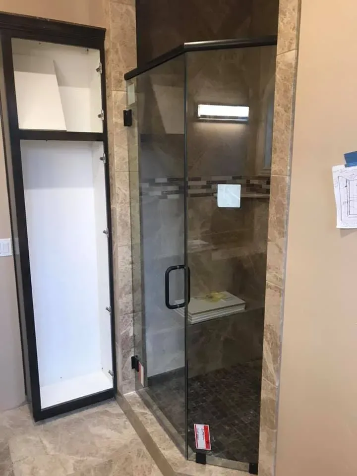 Shower with glass door, adjacent storage cabinet. Tile walls, dark trim, and a built-in seat.