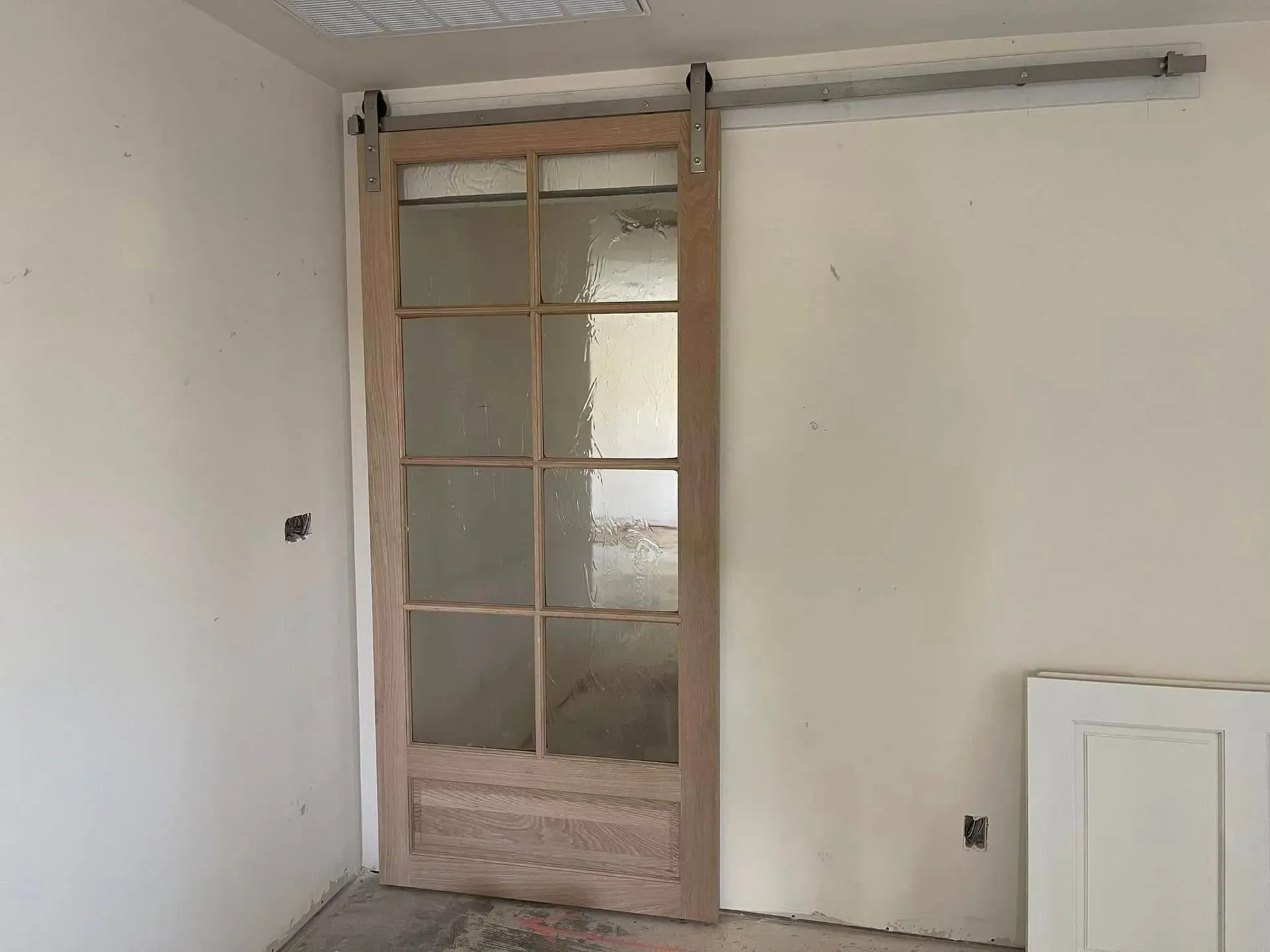 Sliding glass panel door on a silver track, light wood frame, against a light-colored wall.