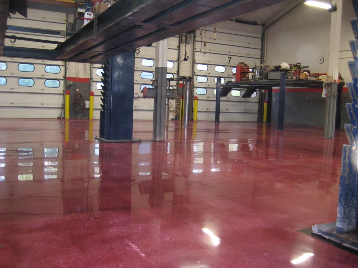 Shiny red epoxy floor in an industrial garage with metal columns and garage doors.