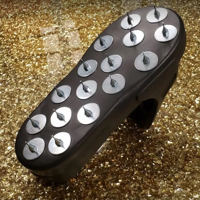 Black oval shoe sole with silver metal studs on a glittery gold background