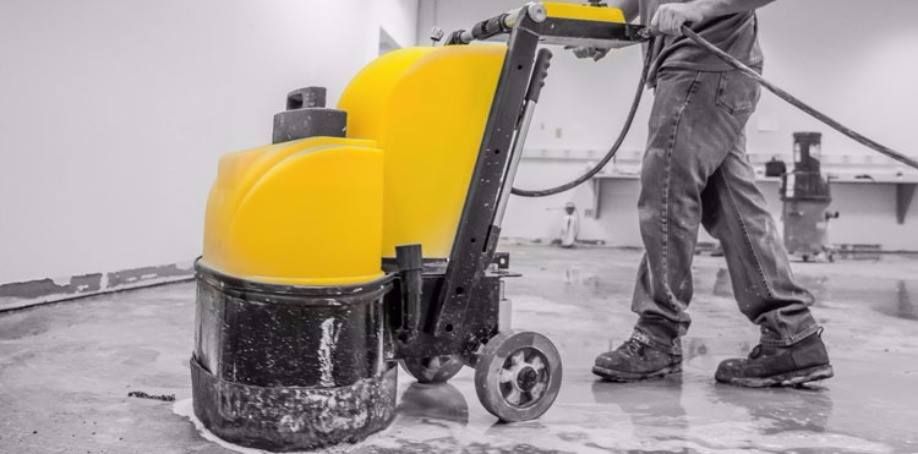 Person using a yellow floor grinder on a concrete surface indoors
