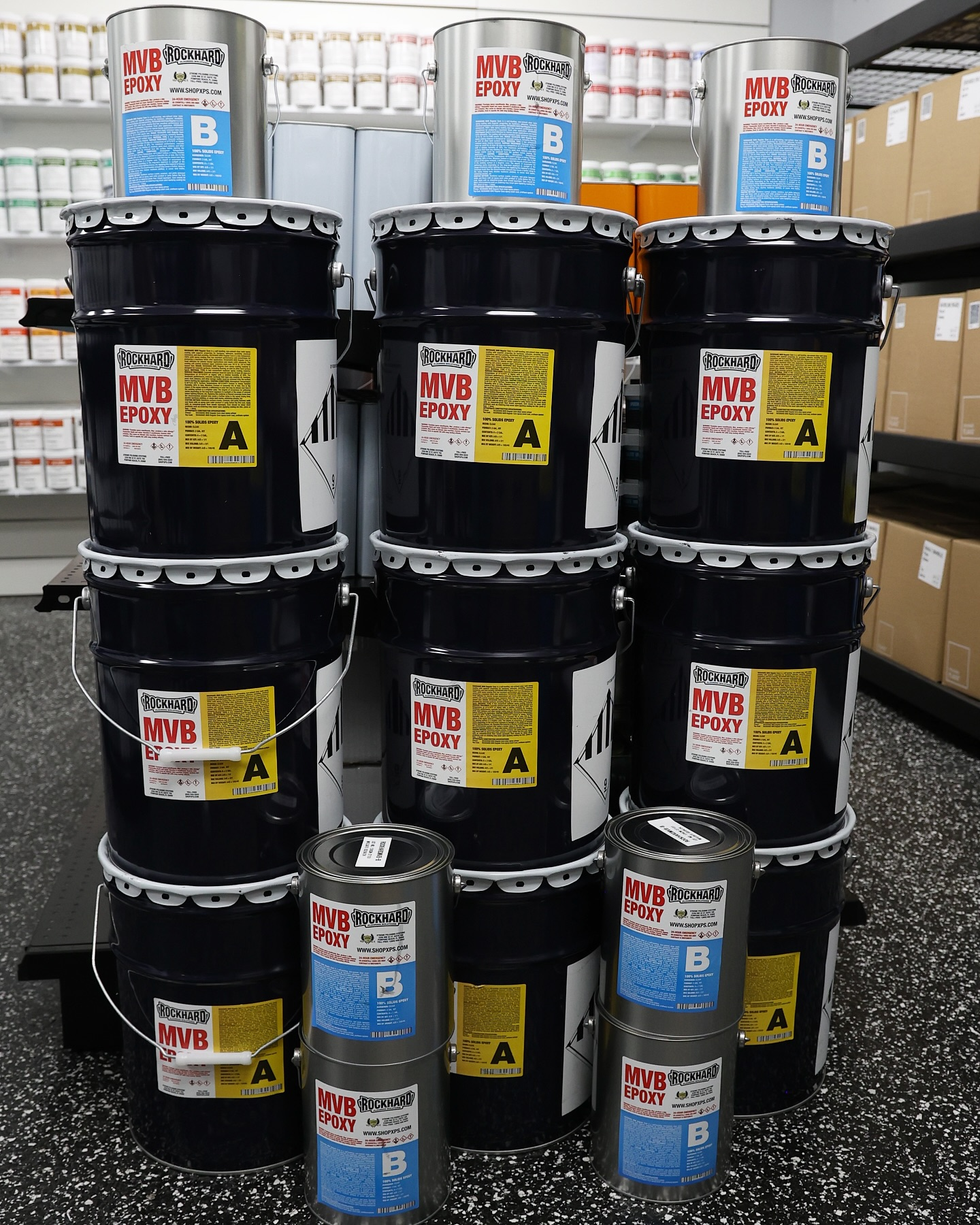 Stacks of black and blue chemical drums in a warehouse aisle
